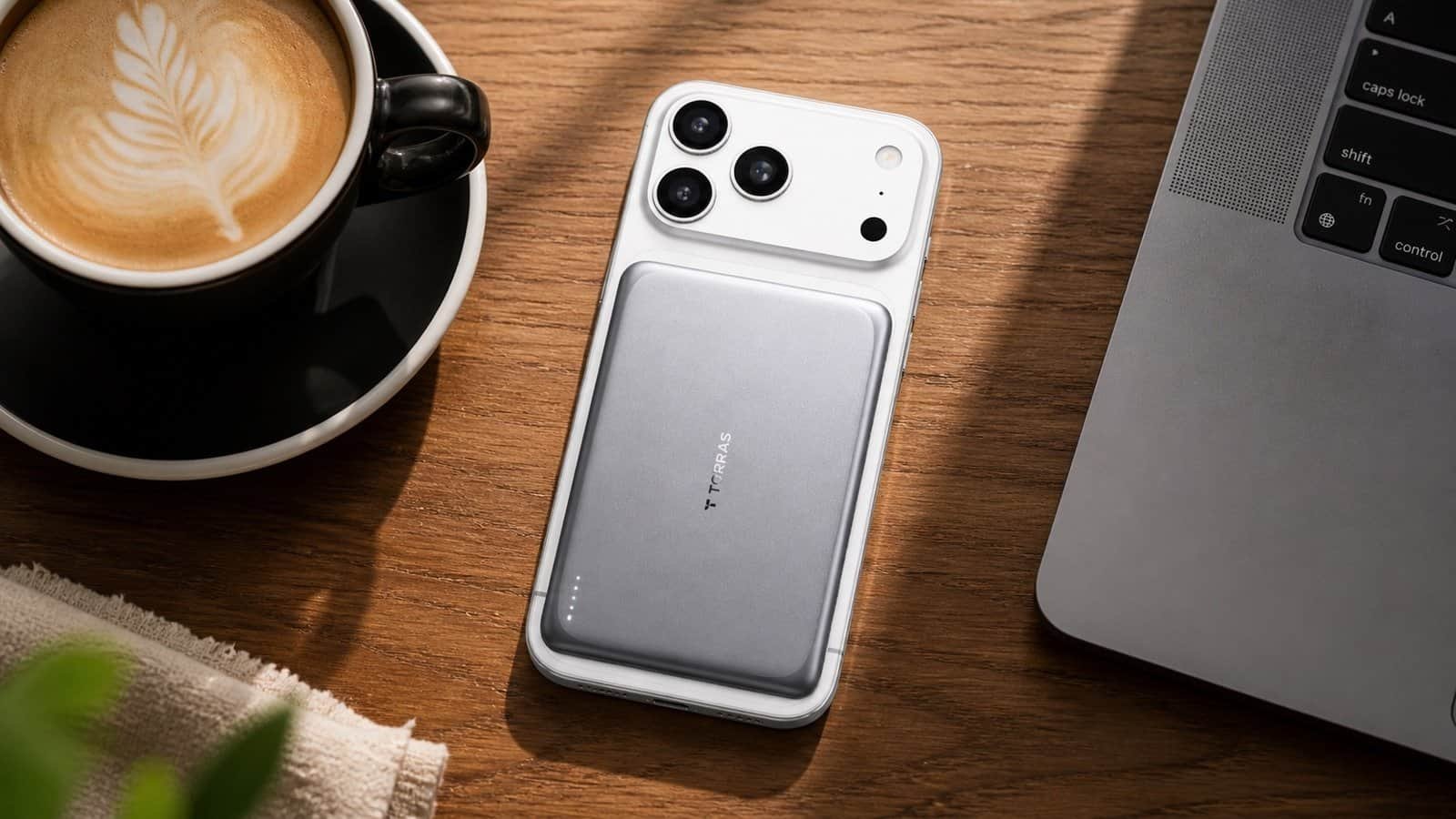 TORRAS MiniMag Pro 5000mAh power bank magnetically attached to back of iPhone via MagSafe on a coffee shop table