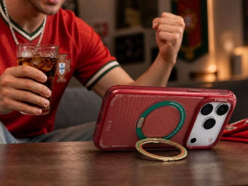 TORRAS x Portuguese Football Federation phone case with a built-in ring stand, propped on a table while a football fan in a red jersey cheers with a cola drink.