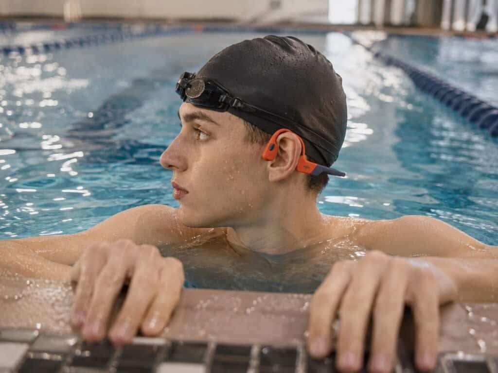 Swimmer wearing Shokz OpenSwim Pro waterproof headphones in an indoor pool